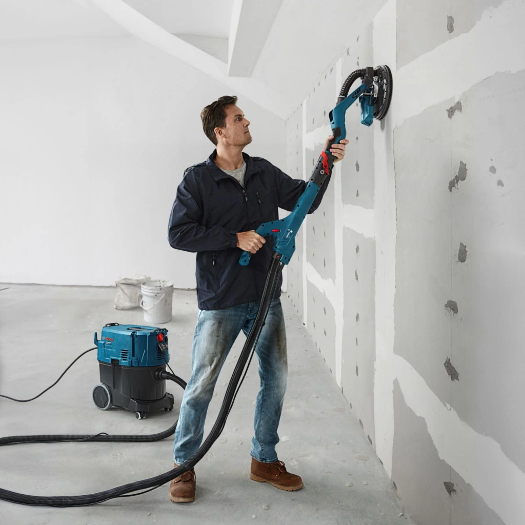 Man is bezig met huren van een Bosch langnekschuurmachine bij BIYU voor efficiënt schuren van wanden, plafonds en vloeren in uw renovatieprojecten.