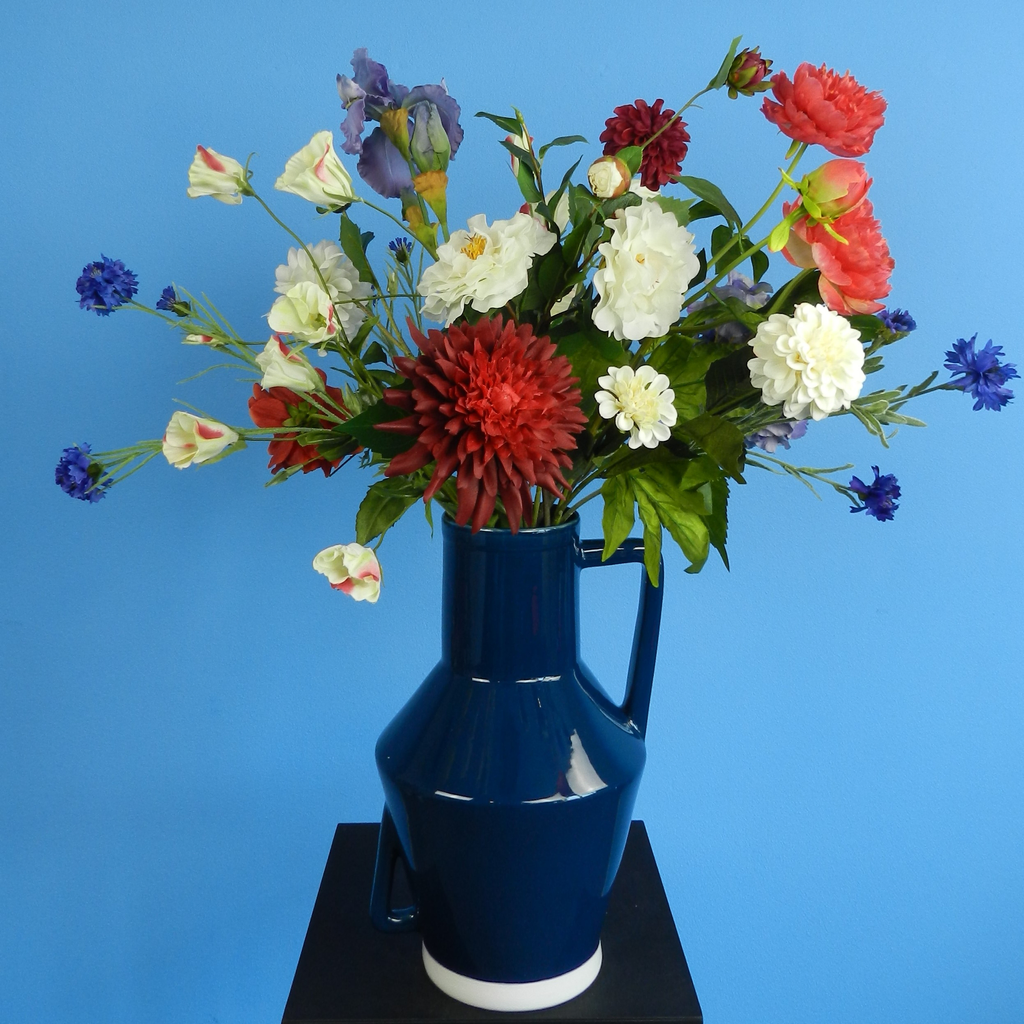 Huur dit prachtige kunstbloemen boeket in blauwe vaas voor jouw evenement bij BIYU. Foto van blauwe groene bladeren en roze bloemen. Perfect als decoratie voor feesten en bruiloften.